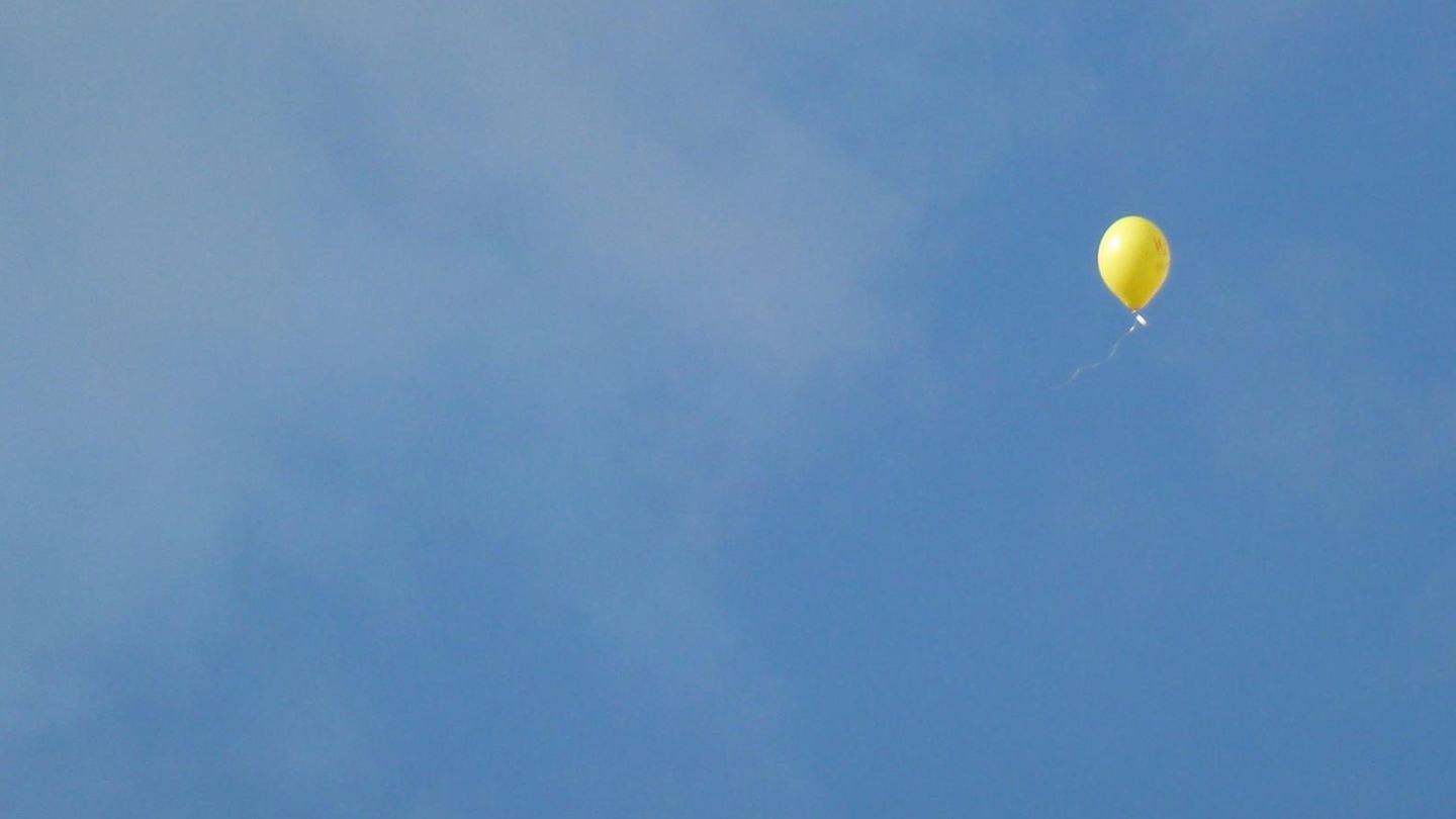 Ein gelber Luftballon schwebt in den Himmel
