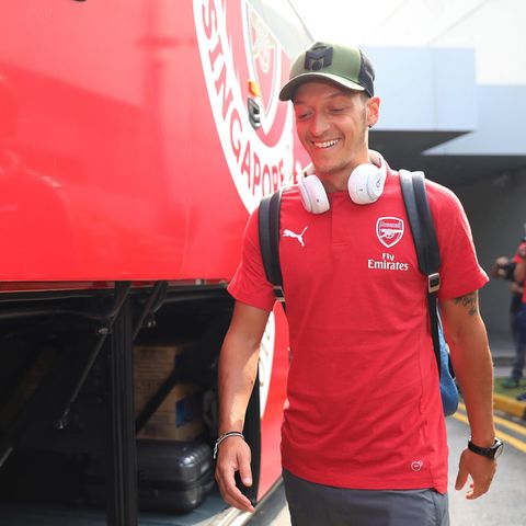 Mit grünem Cap und weißen Kopfhörern um den Hals geht Mesut Özil im roten T-Shirt mit Arsenal-Wappen an einem Bus vorbei