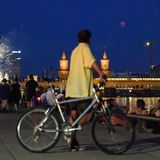 Der Vollmond taucht über der Oberbaumbrücke über der Spree auf, während Berliner sich am Spreeufer ein Feuerwerk anschauen