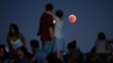 München, Bayern: Zahlreiche Menschen beobachten am Olympiaberg die Mondfinsternis mit dem rötlichen Vollmond