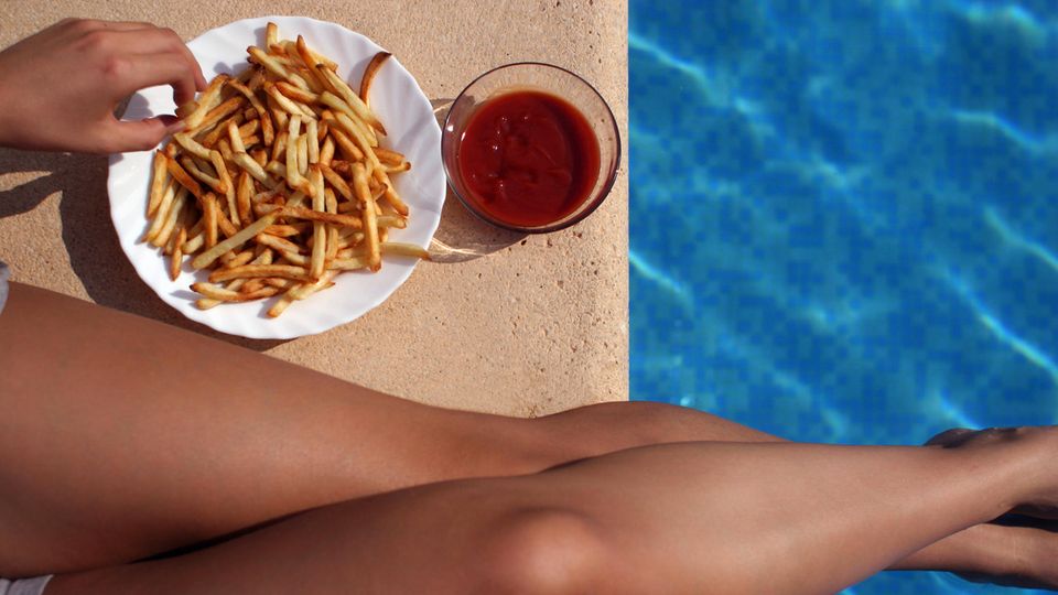 Pommes Schwimmbad Frau Neben Frauenbeinen am Beckenrand steht ein Teller mit Pommes und daneben eine Schale Ketchup. Eine Hand greift Pommes