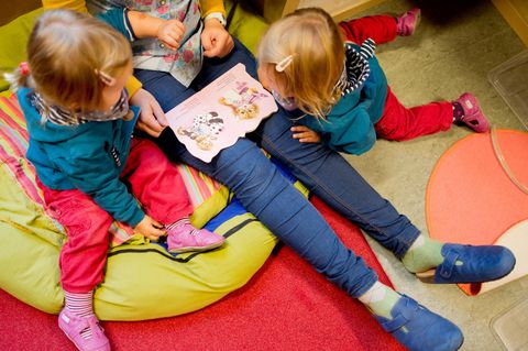 Eine Erzieherin liest mit Zwillingen ein Buch.