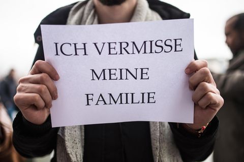 Ein Mann hält sich ein DinA4-Blatt mit dem Satz "Ich vermisse meine Familie" vor die Brust