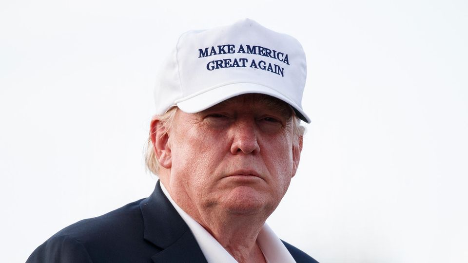 US-Präsident Donald trump steht im Freien und trägt zu Jackett und offenem Hemd ein weißes Cap mit "Make America great again"