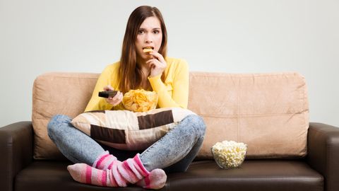 Eine junge Frau sitzt auf dem Sofa und isst Kartoffelchips