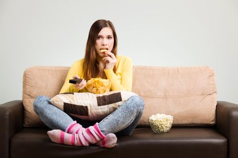 Eine junge Frau sitzt auf dem Sofa und isst Kartoffelchips