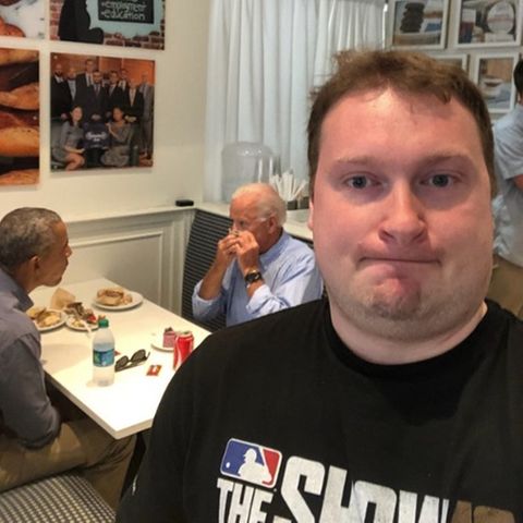 Das Selfie eines Mannes in einer Bäckerei. Im Hintergrund sitzen Joe Biden und Barack Obama an einem Tisch