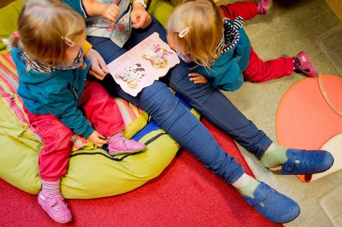 Kinder schmökern mit ihrer Kita-Erzieherin in einem Bilderbuch