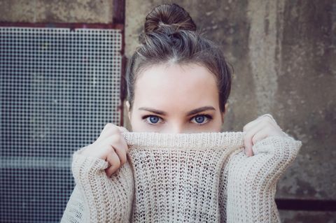 Eine junge Frau, die sich ihren Pulloverkragen über die Nase zieht