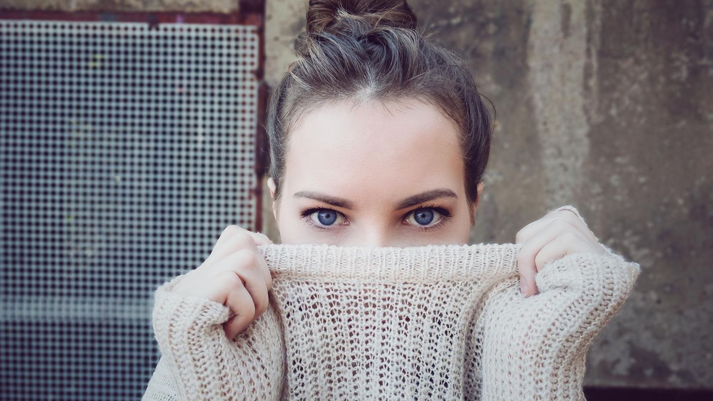 Eine junge Frau, die sich ihren Pulloverkragen über die Nase zieht