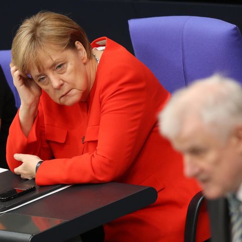 Im Bundestag stützt Angela Merkel ihren Kopf auf, während Horst Seehofer im Vordergrund am Rednerpult steht
