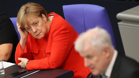 Im Bundestag stützt Angela Merkel ihren Kopf auf, während Horst Seehofer im Vordergrund am Rednerpult steht