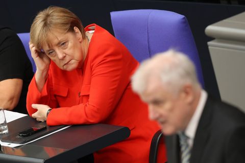 Im Bundestag stützt Angela Merkel ihren Kopf auf, während Horst Seehofer im Vordergrund am Rednerpult steht