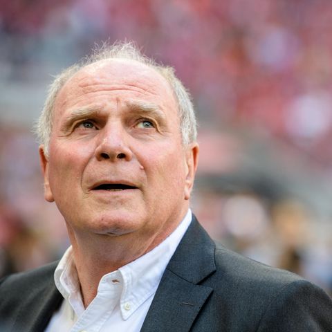 Uli Hoeneß steht in einem Stadion und blickt nach links oben