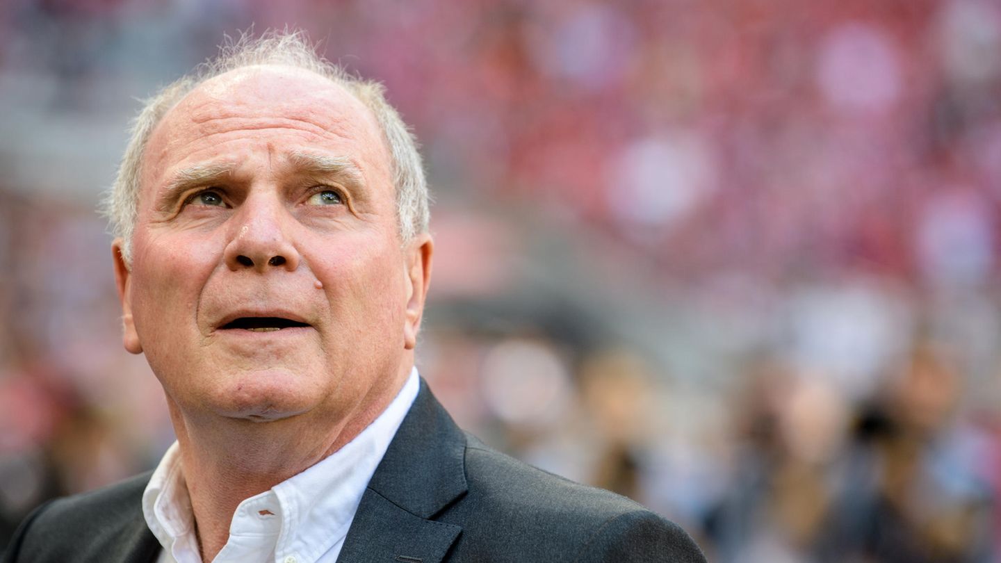 Uli Hoeneß steht in einem Stadion und blickt nach links oben