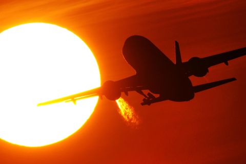 Ein Flugzeug hebt ab. Es fliegt in einen von der Sonne geröteten Himmel hinein