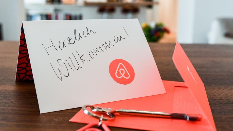 Ein Schlüssel mit einem Airbnb-Anhäger und eine Herzlich-Willkommen-Karte liegen in der Wohnung eines  Gastgebers.