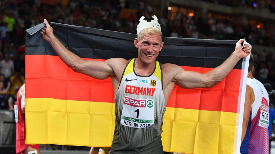 Zehnkämpfer Arthur Abele jubelt mit einer Pappkrone auf dem Kopf und einer Deutschland-Flagge in den ausgebreiteten Armen