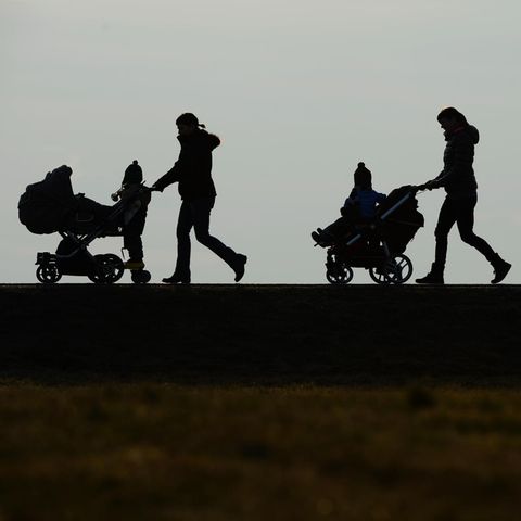 Im Gegenlicht sind die Umrisse dreier Frauen mit Kinderwagen zu sehen. Sie schieben ihre Kinder von rechts nach links