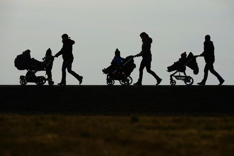 Im Gegenlicht sind die Umrisse dreier Frauen mit Kinderwagen zu sehen. Sie schieben ihre Kinder von rechts nach links