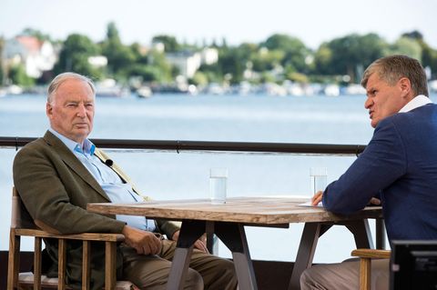 An einem Holztisch sitzen Alexander Gauland von der AfD und Journalist Thomas Walde von ZDF. Im Hintergrund glänzt ein See