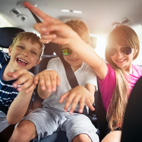 Drei Kinder sitzen auf der Rückbank eines Autos und machen Star-Posen