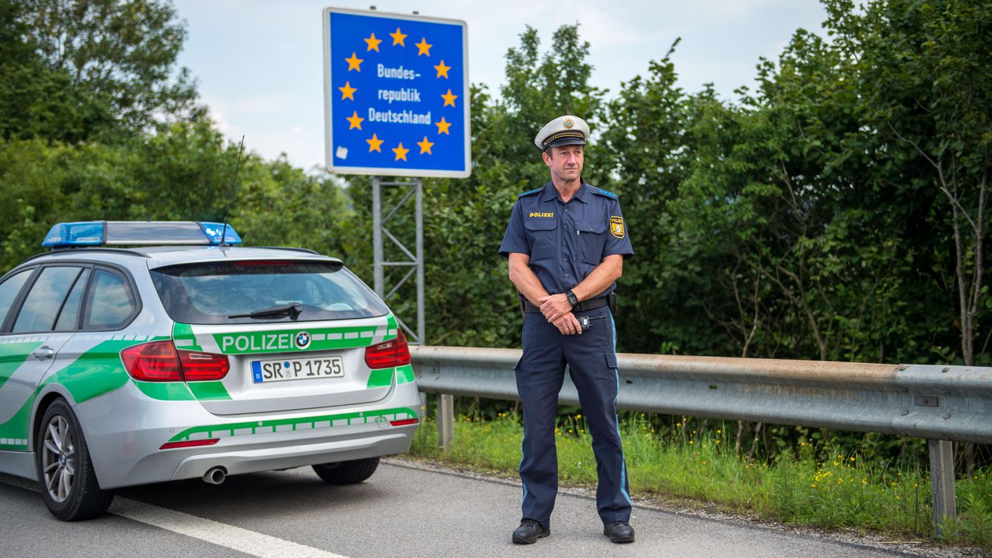 Ein Beamter der bayerischen Grenzpolizei steht hinter seinem Dienstwagen an einem Grenzübergang