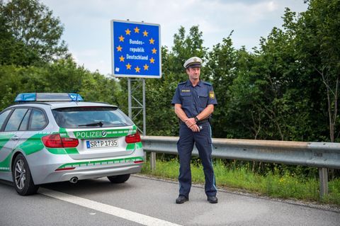 Ein Beamter der bayerischen Grenzpolizei steht hinter seinem Dienstwagen an einem Grenzübergang