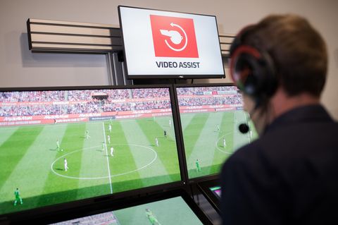 Der Video-Schiedsrichter sitzt vor vier Monitoren auf denen Fußball läuft