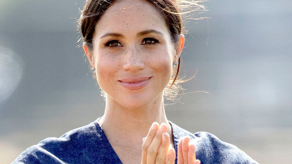 Im blauen Sommerkleid lächelt Herzogin Meghan von Sussex und klatscht in die Hände