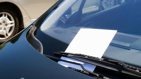Hinter dem Scheibenwischer eines Autos klemmt eine Notiz