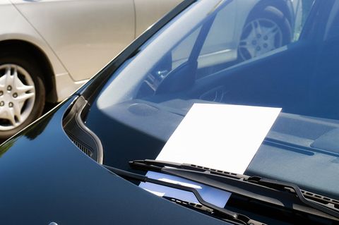 Hinter dem Scheibenwischer eines Autos klemmt eine Notiz