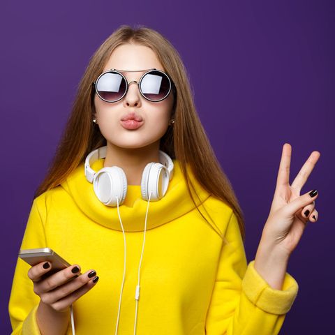 Eine Frau in gelbem Pulli zeigt ein "Peace"-Zeichen in die Kamera.