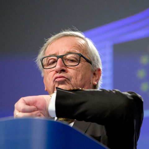 Jean-Claude Juncker schaut im vor einer projezierten EU-Flagge auf die Uhr an seinem linken Handgelenk