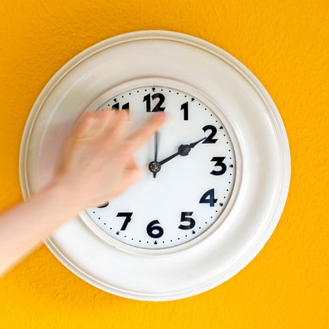 Eine Frau stellt an einer Wanduhr die Zeit um