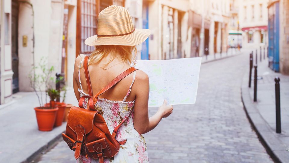 Frau mit Strohhut steht in einer schmalen Gasse und schaut auf eine Landkarte