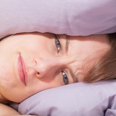 Eine Frau liegt mit gerunzelter Stirn zwischen zwei Kissen