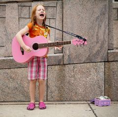 Mächen mit Guitarre singt auf der Straße