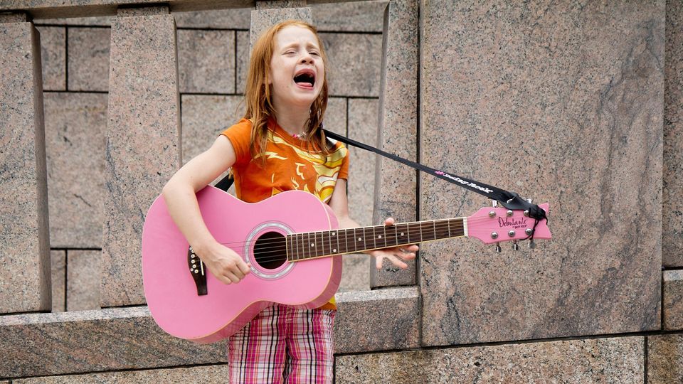 Mächen mit Guitarre singt auf der Straße
