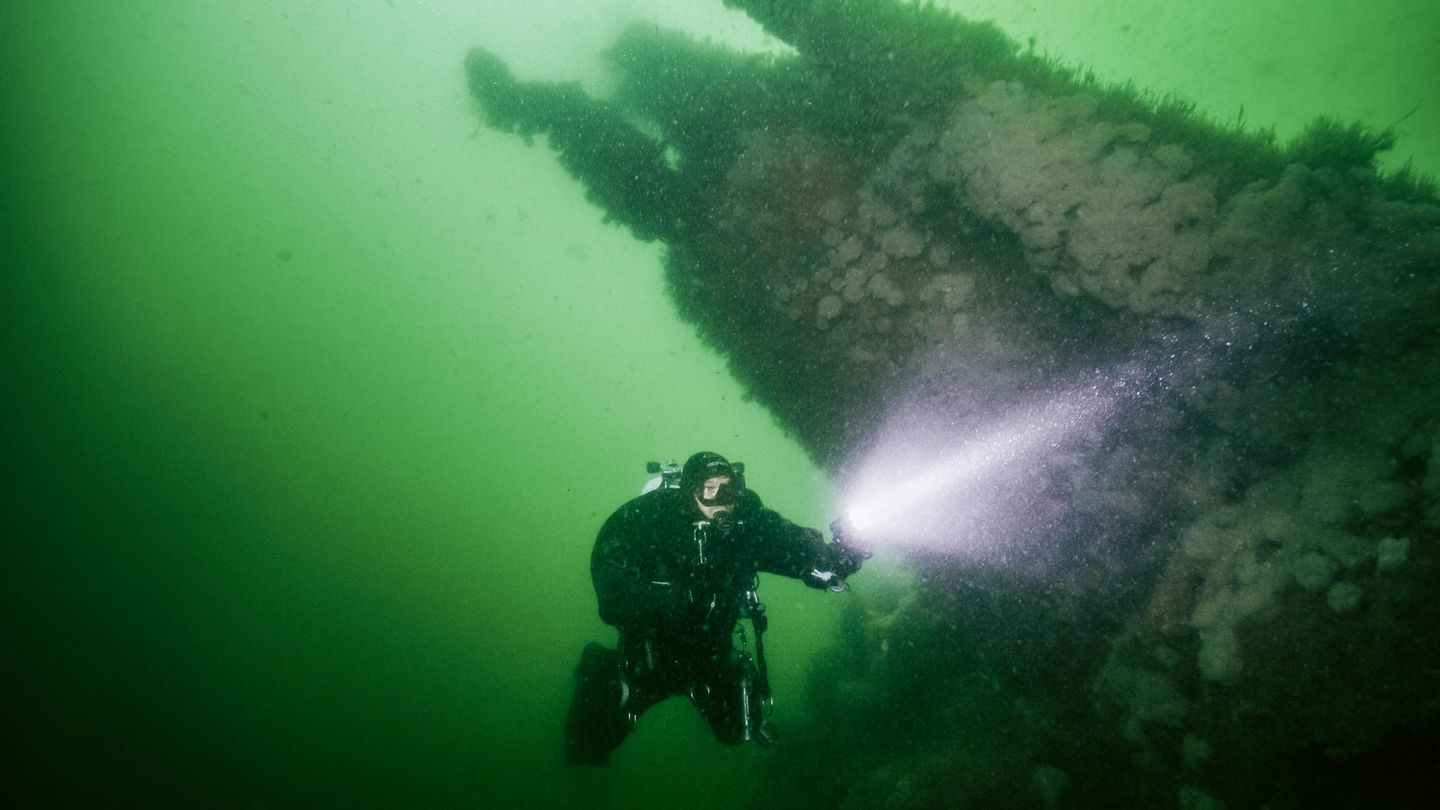Andi taucht mit Taschenlampe durch die grün-schimmernde Nordsee.