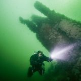 Andi taucht mit Taschenlampe durch die grün-schimmernde Nordsee.