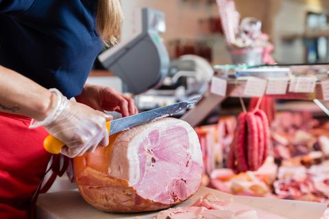 Frau schneidet ein Stück Schinken ab
