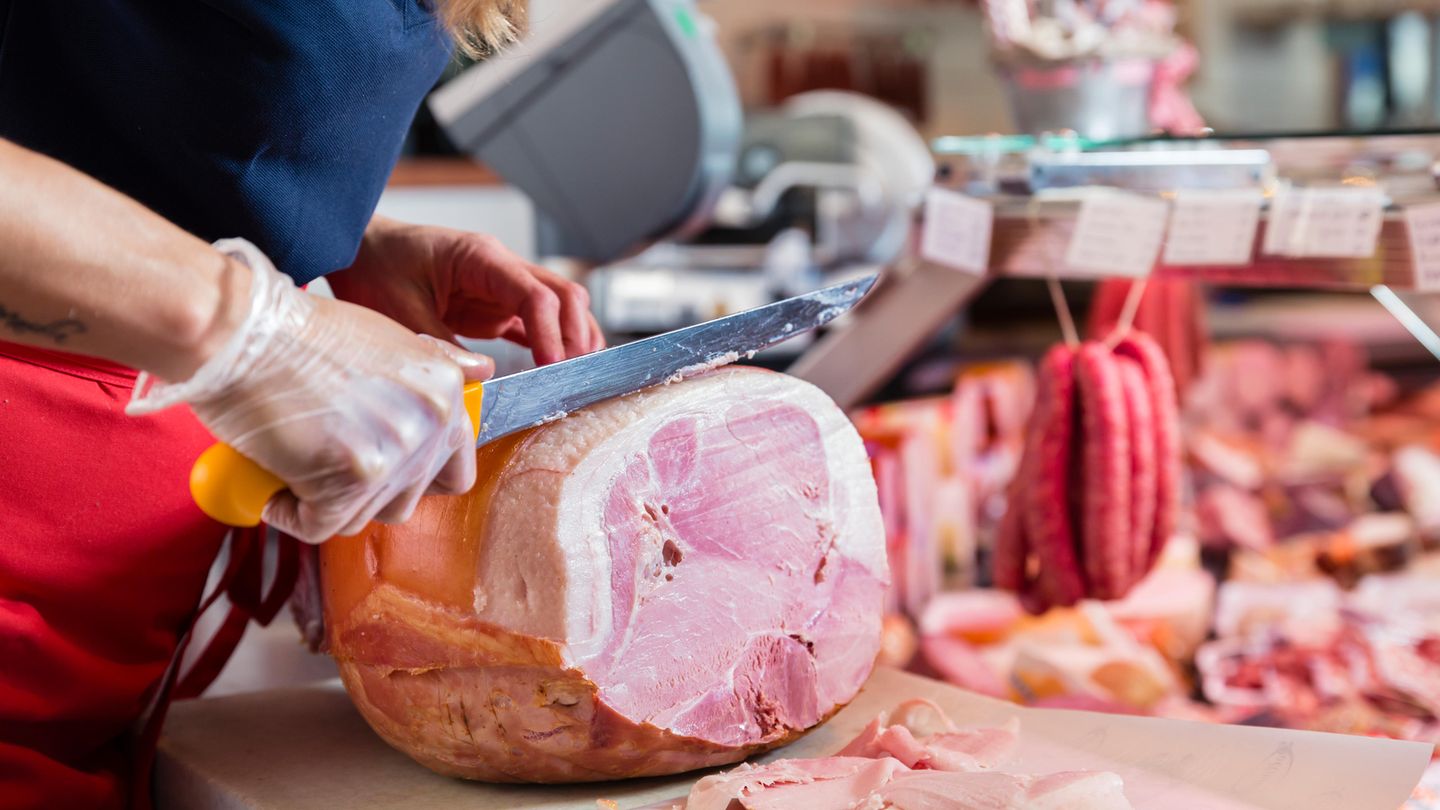 Frau schneidet ein Stück Schinken ab