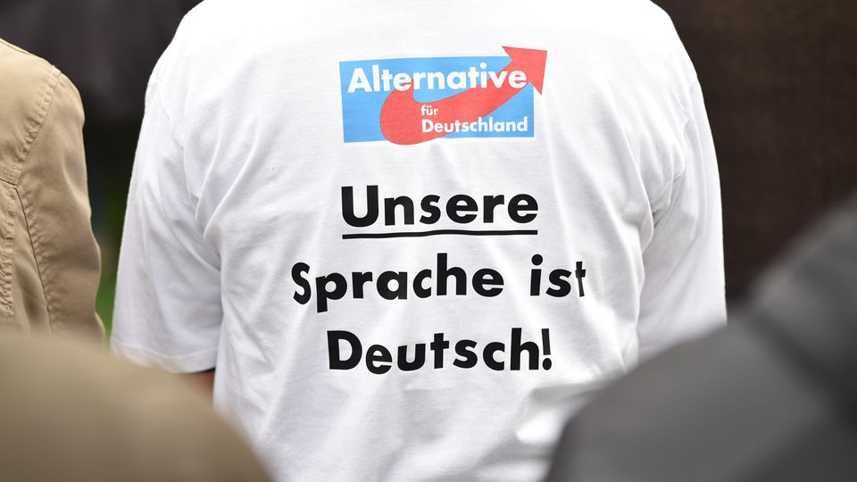 Ein Anhänger der AfD mit dem Aufdruck "Unsere Sprache ist Deutsch!" sitzt während der Rede des Parteivorsitzenden Meuthen beim politischen Frühschoppen auf dem Volksfest Gillamoos auf einer Bank