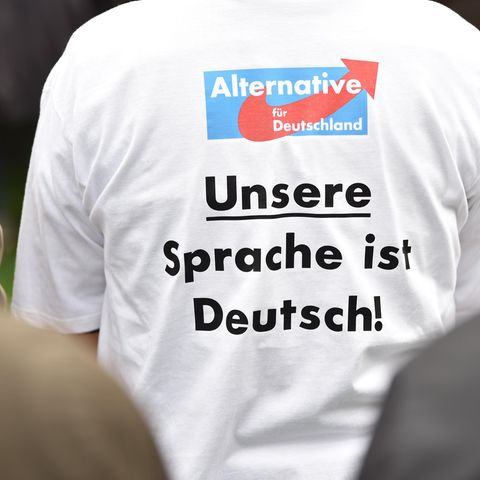Ein Anhänger der AfD mit dem Aufdruck "Unsere Sprache ist Deutsch!" sitzt während der Rede des Parteivorsitzenden Meuthen beim politischen Frühschoppen auf dem Volksfest Gillamoos auf einer Bank