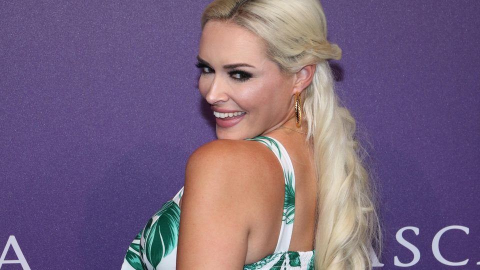 Vor einer violetten Wand lächelt Daniela Katzenberger über ihre linke Schulter in die Kameras. Sie trägt ein Top und eine Hose