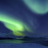 Polarlicht über Fjord in winterlicher Landschaft in Sommeroya bei Tromsø