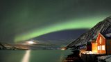 Eine rote Fischerhütte am Fjord mit Polarlicht in Sommeroya bei Tromsø: Mindestens ein Loch in der Wolkendecke ist nötig, um das Leuchten zu sehen.