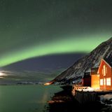 Eine rote Fischerhütte am Fjord mit Polarlicht in Sommeroya bei Tromsø: Mindestens ein Loch in der Wolkendecke ist nötig, um das Leuchten zu sehen.