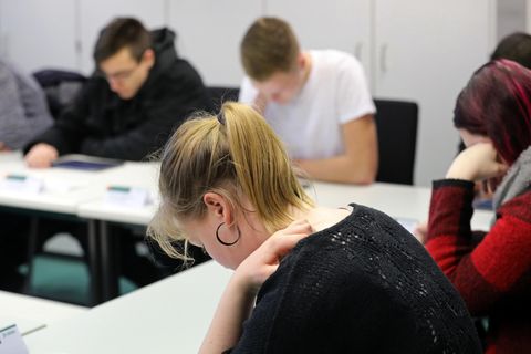 Zwei junge Frauen und zwei junge Männer sitzen über ihrer Theorieprüfung für den Führerschein gebeugt